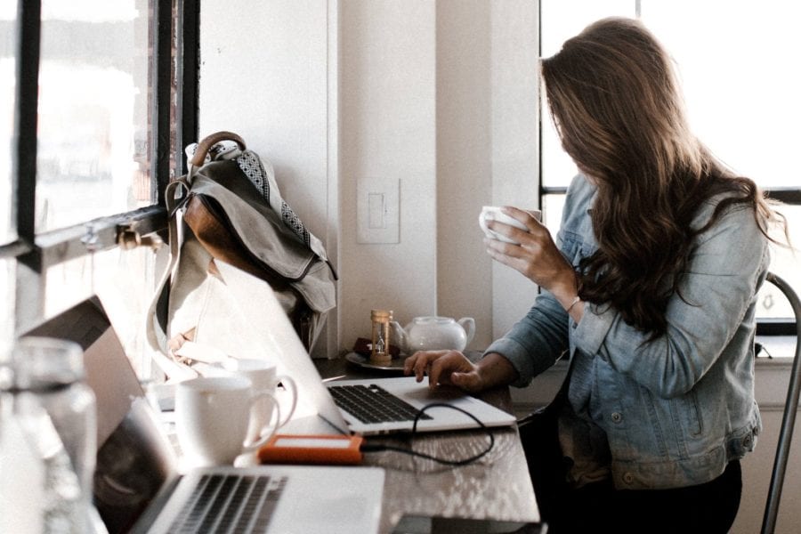 Businesswoman sips coffee while researching customer retention techniques on laptop
