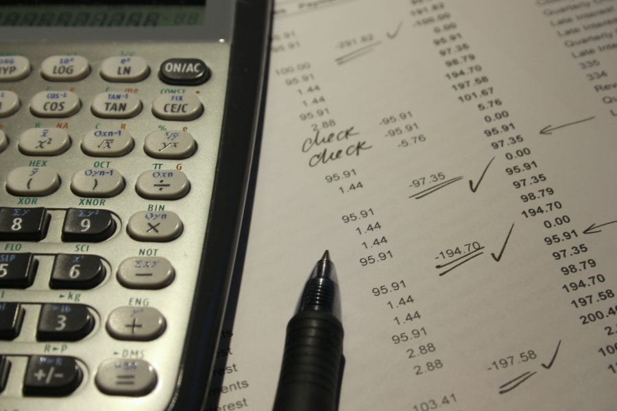 A calculator and statement with a pen which is being used to check off bank entries