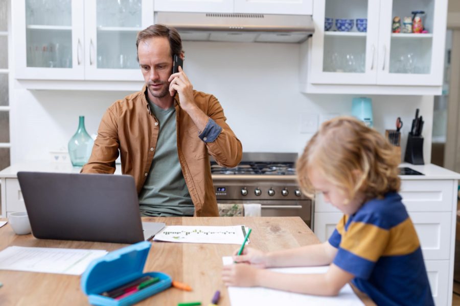 Father attempts to work from home during lockdown while child colours next to him