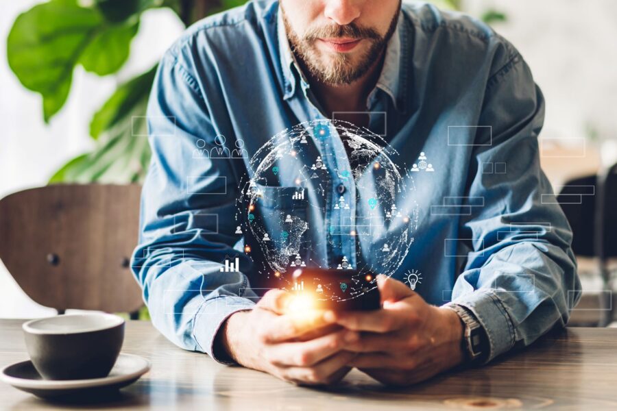 Photograph of a man sitting at a table holding a smartphone with a digital globe and a data visualisation hologram projecting above the device.